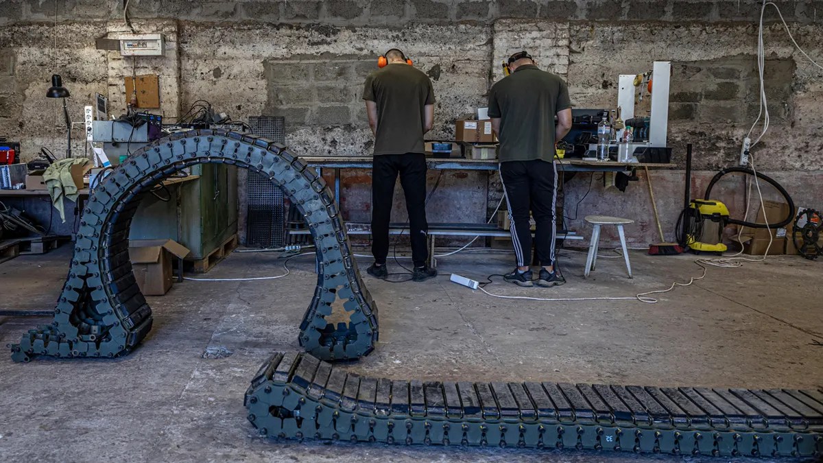 Engineers of design and production bureau "UkrPrototyp" work on new parts for a ground drone at a table next to large treads for one of the drones.